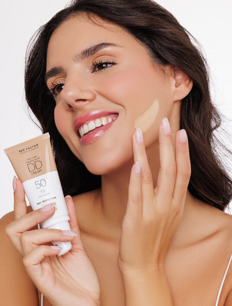 Γυναίκα με την 5 in 1 DD Κρέμα Προσώπου SPF50 από την Bee Factor, αποχρώση 02, εφαρμόζει την κρέμα στο πρόσωπό της για προστασία από UVB και μπλε φως. Διαθέσιμη στο Eiria Cosmetics.