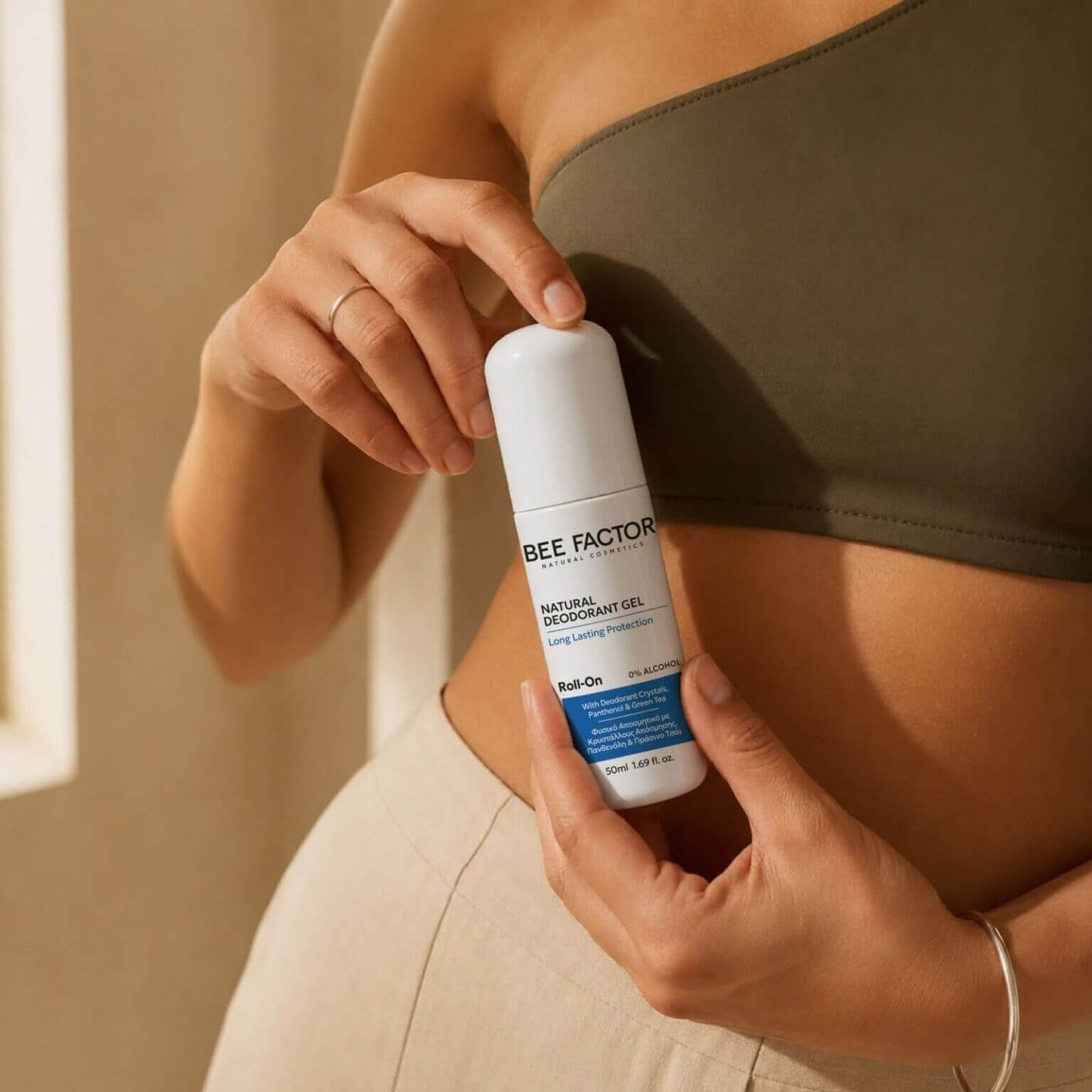 Γυναίκα κρατά το Bee Factor Natural Deodorant Gel φυσικό αποσμητικό σώματος Roll-On 50ml, με λευκή συσκευασία, μαύρα γράμματα και μπλε ετικέτα. Lifestyle παρουσίαση του αποσμητικού με κρυστάλλους απόσμησης, πανθενόλη και πράσινο τσάι, 0% alcohol, για καθημερινή φροντίδα, φρεσκάδα και προστασία από την κακοσμία μεγάλης διάρκειας.