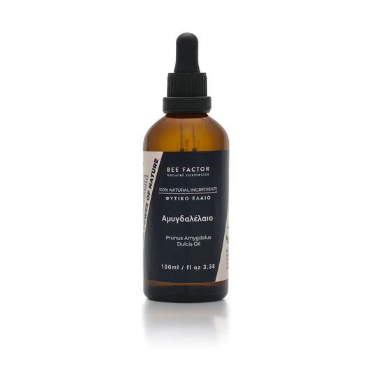 Το αμυγδαλέλαιο της Bee Factor Natural Cosmetics σε κεχριμπαρένια γυάλινη φιάλη 100 ml με μαύρο σταγονόμετρο, σχεδιασμένο με minimal και επαγγελματική αισθητική. Στην μπροστινή ετικέτα διακρίνονται το λογότυπο “Bee Factor natural cosmetics”, η ένδειξη “100% natural ingredients”, η κατηγορία «φυτικό έλαιο», η ονομασία «Αμυγδαλέλαιο» και η λατινική ονομασία “Prunus Amygdalus Dulcis Oil”. Το προϊόν απεικονίζεται μετωπικά, μόνο του, σε καθαρό ανοιχτόχρωμο φόντο, αποπνέοντας αίσθηση φυσικότητας, καθαρότητας και 