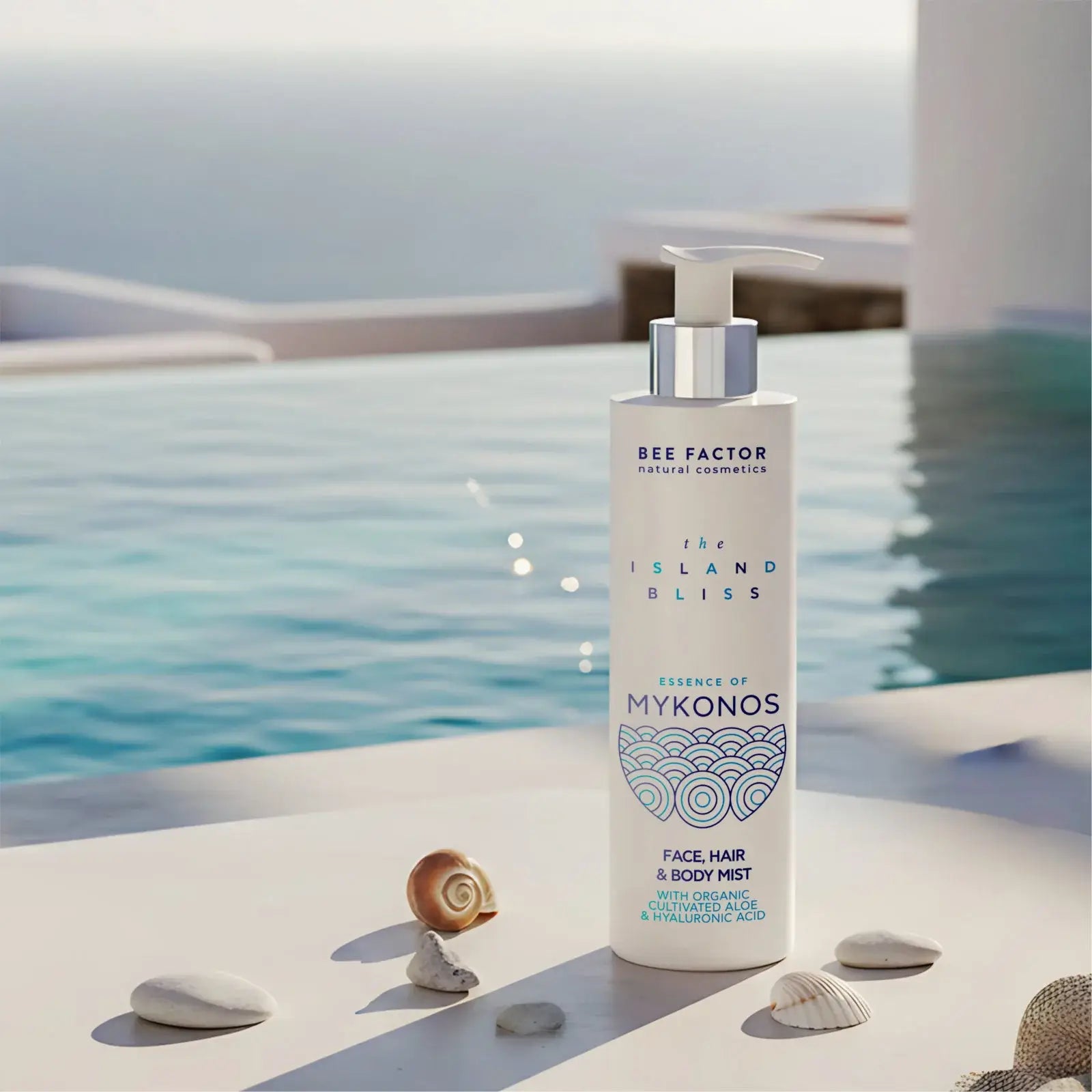 Προωθητική εικόνα του Essence of Mykonos Face, Hair & Body Mist από τη συλλογή The Island Bliss της Bee Factor Natural Cosmetics, με τη λευκή φιάλη με αντλία να τοποθετείται σε φωτεινή λευκή επιφάνεια δίπλα σε πισίνα, με φόντο που παραπέμπει σε πολυτελές κυκλαδίτικο περιβάλλον. Στη συσκευασία διακρίνονται το λογότυπο “Bee Factor natural cosmetics”, η ονομασία της σειράς “The Island Bliss”, η ένδειξη “Essence of Mykonos” και η κατηγορία “Face, Hair & Body Mist”, μαζί με αναφορά σε organic cultivated aloe και