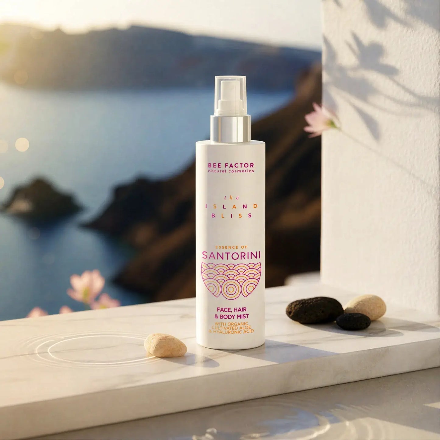 Προωθητική εικόνα του Essence of Santorini Face, Hair & Body Mist από τη συλλογή The Island Bliss της Bee Factor Natural Cosmetics, με τη λευκή φιάλη spray τοποθετημένη πάνω σε φωτεινή μαρμάρινη επιφάνεια μπροστά από εντυπωσιακή θέα θάλασσας και βραχώδους τοπίου που παραπέμπει στη Σαντορίνη. Στη συσκευασία διακρίνονται το λογότυπο “Bee Factor natural cosmetics”, η ονομασία της σειράς “The Island Bliss”, η ένδειξη “Essence of Santorini” και η κατηγορία “Face, Hair & Body Mist”, μαζί με αναφορά σε organic cul