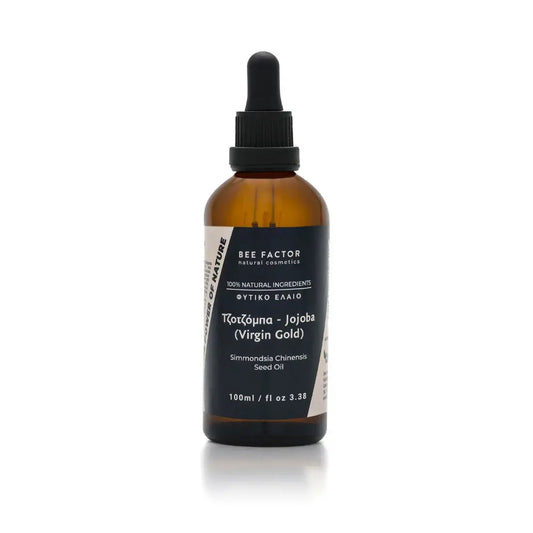 Το έλαιο τζοτζόμπα Jojoba Virgin Gold της Bee Factor Natural Cosmetics σε κεχριμπαρένια γυάλινη φιάλη 100 ml με μαύρο σταγονόμετρο, σχεδιασμένο με minimal και επαγγελματική αισθητική. Στην μπροστινή ετικέτα διακρίνονται το λογότυπο “Bee Factor natural cosmetics”, η ένδειξη “100% natural ingredients”, η κατηγορία «φυτικό έλαιο», η ονομασία «Τζοτζόμπα - Jojoba (Virgin Gold)» και η λατινική ονομασία “Simmondsia Chinensis Seed Oil”. Το προϊόν απεικονίζεται μετωπικά, μόνο του, σε καθαρό ανοιχτόχρωμο φόντο, αποπν