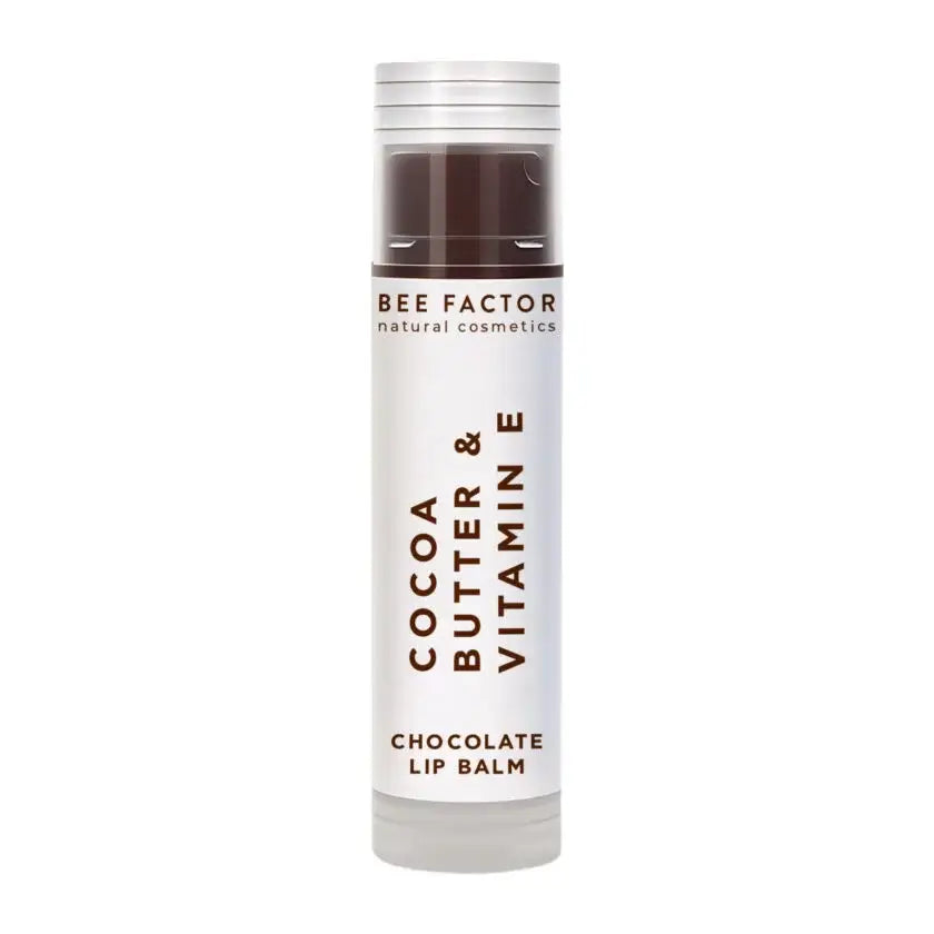 Bee Factor Chocolate Lip Balm με βούτυρο κακάο και βιταμίνη Ε σε πρακτική stick συσκευασία, ιδανικό για ενυδάτωση και καθημερινή φροντίδα των χειλιών. Η συσκευασία είναι λευκή με καφέ λεπτομέρειες, διάφανο καφέ επάνω μέρος και καπάκι σε μεταλλική όψη, ενώ στο σώμα αναγράφονται κάθετα τα στοιχεία “Cocoa Butter & Vitamin E” και χαμηλά η ένδειξη “Chocolate Lip Balm”. Το προϊόν απεικονίζεται μόνο του, σε καθαρό λευκό φόντο.