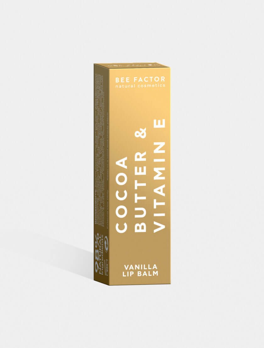 Συσκευασία Lip Balm Vanilla της Bee Factor με χρυσό-μεταλλικό κουτί και έντονα λευκά γράμματα "Cocoa Butter & Vitamin E". Φυσικό ενυδατικό balm χειλιών με 98% φυσικά συστατικά, βούτυρο κακάο και βιταμίνη Ε. Premium σχεδιασμός που υποδηλώνει ποιότητα και φροντίδα, διαθέσιμο στο eiria.gr.