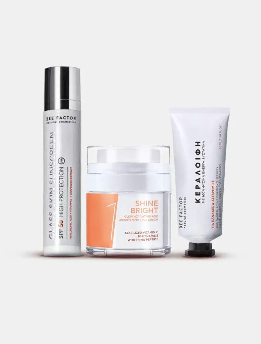 Το Radiant Defense Set της Bee Factor Natural Cosmetics με τρία προϊόντα περιποίησης προσώπου, τοποθετημένα δίπλα δίπλα σε καθαρό ανοιχτόχρωμο φόντο. Στα αριστερά εμφανίζεται το Glass Skin Sunscreen SPF 50 High Protection σε λευκή αεροστεγή συσκευασία με ασημί καπάκι, στο κέντρο η Shine Bright κρέμα προσώπου σε διάφανο βαζάκι με λευκό καπάκι και πορτοκαλί ετικέτα, και στα δεξιά η κεραλοιφή σε λευκή σωληναριακή συσκευασία με μαύρο καπάκι. Η σύνθεση αναδεικνύει ένα ολοκληρωμένο σετ για λάμψη, προστασία και πι