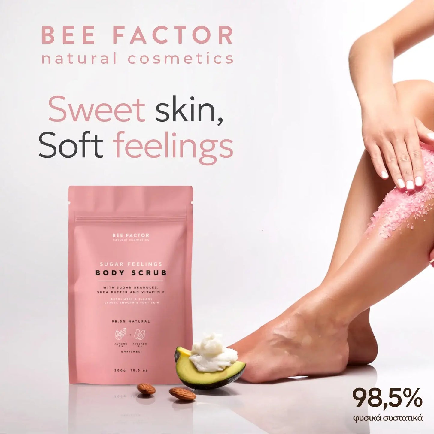 Προωθητική εικόνα του Sugar Feelings Body Scrub της Bee Factor Natural Cosmetics, με τη ροζ συσκευασία του προϊόντος στο αριστερό μέρος και γυναικείο πόδι στο δεξί μέρος, όπου γίνεται εφαρμογή του scrub πάνω στην επιδερμίδα. Στη σύνθεση εμφανίζονται επίσης μισό αβοκάντο με κρεμώδη υφή και αμύγδαλα, στοιχεία που παραπέμπουν στα θρεπτικά έλαια της φόρμουλας, ενώ αναγράφονται το λογότυπο της Bee Factor, το μήνυμα “Sweet skin, Soft feelings” και η ένδειξη “98,5% φυσικά συστατικά”. Η εικόνα αποπνέει αίσθηση απαλ